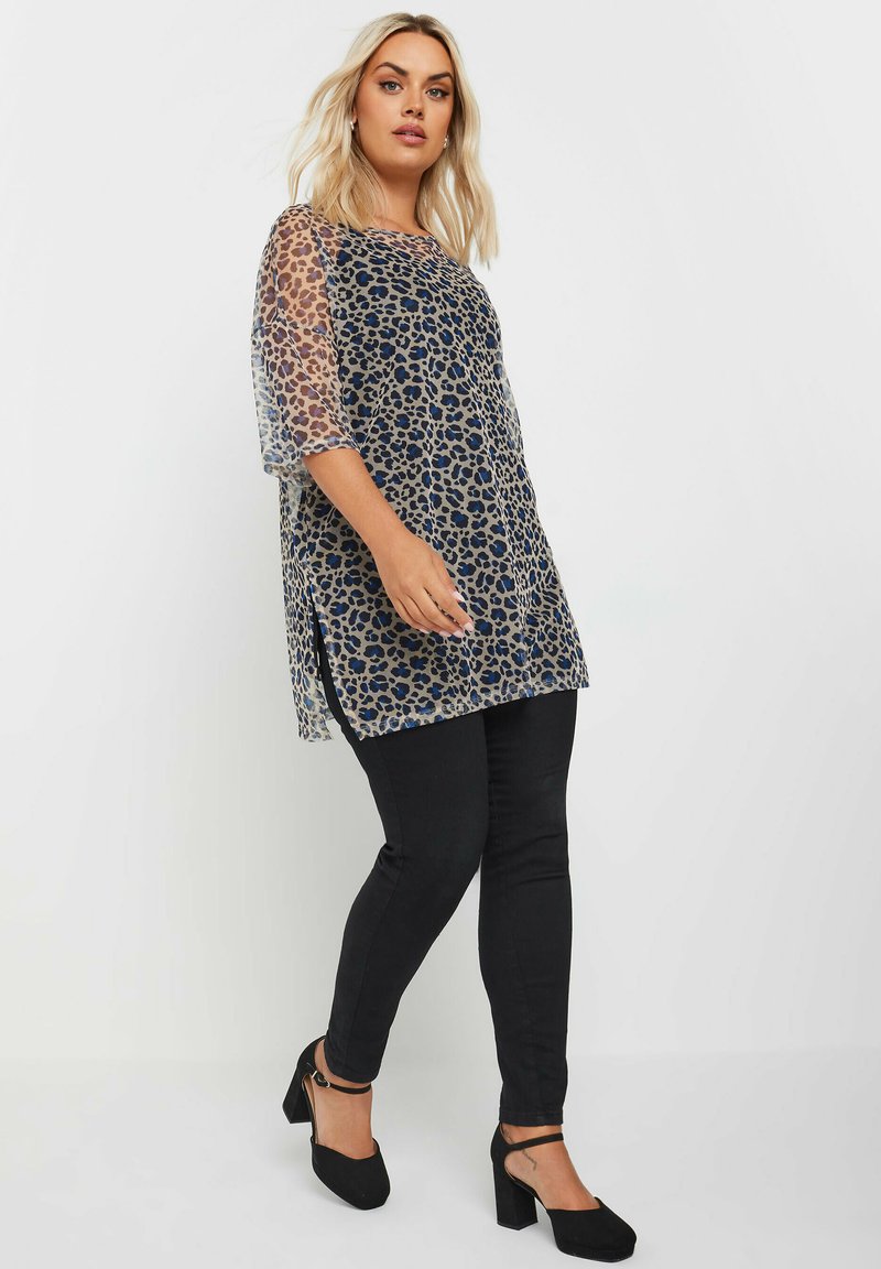 Gennemsigtig leopardprint-top med korte gennemsigtige ærmer, rund halsudskæring, sideslidser og parret med sorte tætsiddende jeans og sorte hæle.