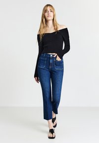 Top nero a costine senza spalle abbinato a jeans in denim blu a vita alta con due tasche posteriori e orli svasati, indossato con sandali neri.