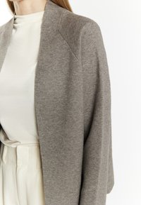 Cardigan de culoare gri deschis, dintr-un amestec de lână, cu croială oversized și deschidere frontală. Are o textură moale și o cădere confortabilă, asociat cu un top ușor.