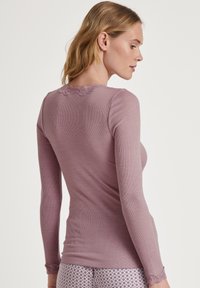 Langermige top in mauve geribbeld materiaal met kantdetails op de halslijn en manchetten. Strak ontwerp, laat een gladde textuur zien.