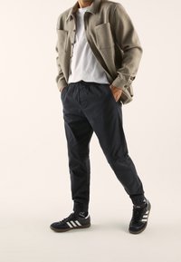 Grey button-up jacket over a white t-shirt, paired with black elastic-waist pants and black sneakers with white stripes.
