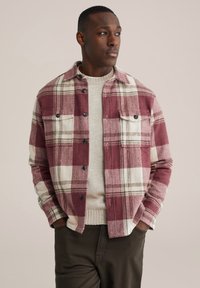 Rot-weiß kariertes Hemdjacke mit Knopfverschluss, Brusttaschen und weicher Stofftextur, getragen über einem leichten Pullover.