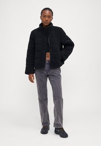 Svart avkortet pufferjakke med en strukturert, fluffy overflate, med høy krage og trykknapper, parret med grå jeans og mørke sneakers.