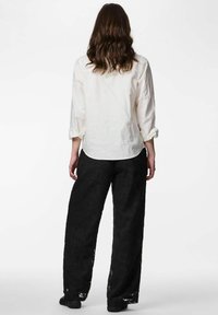 Valge poolläbipaistev nööpidega särk, mille varrukad on üles keeratud, kombineeritud musta pitsiga laia säärega pükstega, millel on lillemustrid. Tavalised mustad jalatsid.