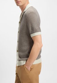 Cardigan a maniche corte con motivo strutturato marrone e crema, con collo e bottoni color crema chiaro, abbinato a pantaloni color cuoio.