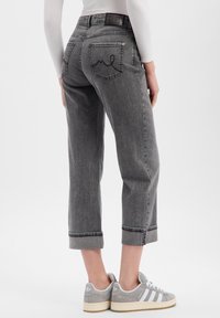 Jean denim gris avec une coupe décontractée, longueur raccourcie et revers retroussés. Comprend des poches arrière avec un motif de surpiqûres décoratives.