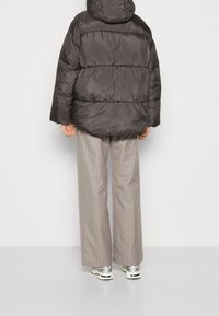 Chaqueta con capucha negra y acolchada de textura brillante, combinada con pantalones de pierna ancha de rayas finas en gris claro y zapatillas metálicas.