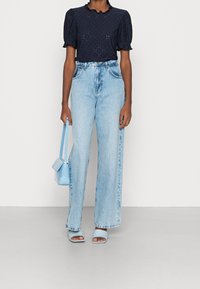 Marinblus med kort längd och puffärmar, matchad med ljusblå högmidjade jeans. Accessoarer inkluderar en ljusblå handväska och matchande sandaler.