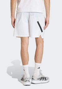 Λευκά αθλητικά σορτς με μαύρη πλαϊνή ρίγα και χωρισμένο τελείωμα. Φορεμένα με λευκές κάλτσες και γκρι αθλητικά παπούτσια. Ομαλή υφή υφάσματος.