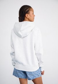 Lys grå hettegensser laget av myk stoff med en avslappet passform. Har en kengurulomme og ribbede mansjetter, kombinert med denimshorts.