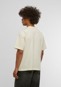 Krémové tričko s krátkým rukávem, kulatým výstřihem, vyrobené z bavlny, volného střihu a viditelnými švy, spárované s tmavými džíny.