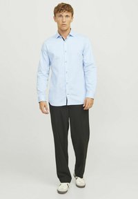 Chemise bleu clair à manches longues avec boutons noirs, assortie à un pantalon noir et des baskets blanches. Texture lisse, col standard.