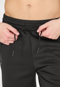 Svarta joggingbyxor med elastisk midja och dragsko. Tyget har en slät struktur och sitter bekvämt vid midjan.