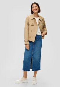 Beige cropped trenchcoat met dubbele knopen, gecombineerd met een blauwe denim midi-rok met een voorkant split en witte sneakers.
