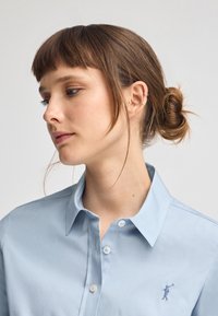Camicia azzurra chiaro con bottoni realizzata in tessuto liscio, dotata di un logo ricamato discreto sul petto e di un design colletto classico.