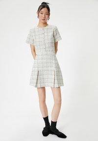 Vestido de tweed en blanco con motas negras, de mangas cortas, cuello redondo, cierre de botones en la parte delantera y detalles de falda plisada.