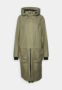 Długi oliwkowy płaszcz przeciwdeszczowy z kapturem, z przednim zapięciem na zamek, dwiema dużymi kieszeniami i czarnymi mankietami. Gładki, wodoodporny materiał.