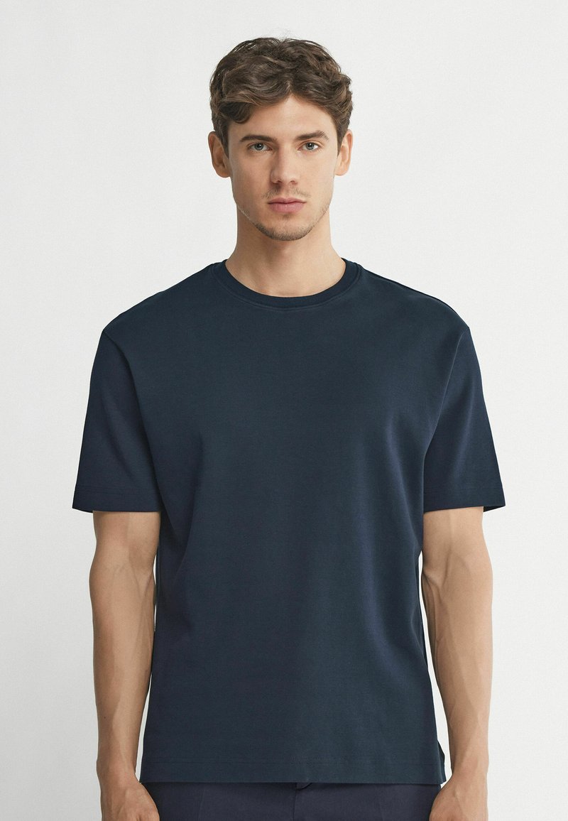 Mörkblå bomullströja med korta ärmar, rundad hals och en enkel design. Mjuk textur och rak skärning. Inga synliga mönster eller detaljer.