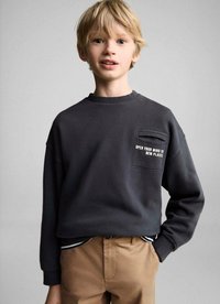 Sweat-shirt gris foncé avec un col rond, doté d'une poche sur la poitrine. Le texte indique "OUVRE TON ESPRIT À DE NOUVELLES PLACES." Associé à un pantalon beige.