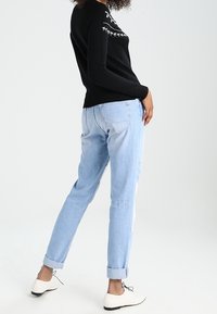 Pull en tricot noir avec un motif géométrique blanc, associé à un jean en denim bleu clair. Des chaussures blanches complètent la tenue.