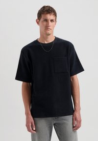 Černé fleece tričko s krátkými rukávy, kulatým výstřihem a kapsou na prsou, v kombinaci s světle šedými džíny. Hladká textura.