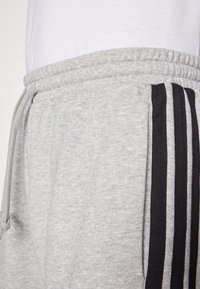 Γκρι φόρμες με κορδόνι στη μέση, δύο πλαϊνές τσέπες και τρεις μαύρες ρίγες κατά μήκος των πλευρών. Μαλακή υφή, casual σχεδίαση.