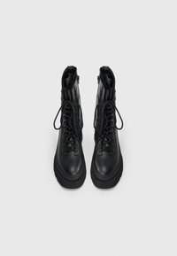 Ein Paar schwarze Leder-Schnürkampfstiefel mit dicken Sohlen, seitlichen Reißverschlüssen und knöchelhohem Design auf weißem Hintergrund.
