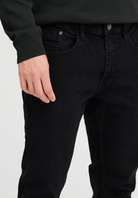 Svarta denimjeans med slim fit, femficksdesign och metallbeslag. Texturen ser slät ut med en svag lyster.