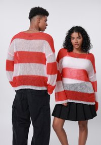 Maglione oversize a strisce rosse e bianche con maniche lunghe, caratterizzato da una finitura testurizzata. Abbinato a pantaloni cargo neri e una gonna plissettata.
