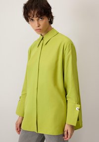 Roheline puuvillane särk terava krae, pikkade varrukate ja nööbitavate mansettidega. Omaduseks on lõdvestunud lõige ja sile tekstuur.