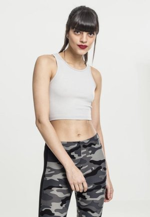 Hvit avkortet tanktopp paret med grå kamuflasje leggings, som fremhever et tettsittende design og glatt tekstur. Klare detaljer av kontrasterende mønstre.