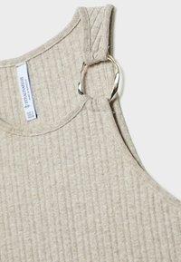 Haut sans manches en tissu beige à côtes avec un anneau métallique argenté torsadé reliant la bretelle.