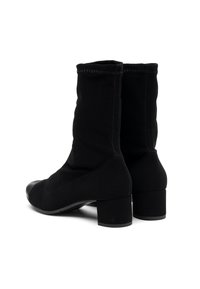 Une paire de bottes noires mi-mollet avec des talons blocs et des bords supérieurs cousus, présentée sous un angle légèrement oblique depuis l'arrière sur un fond blanc.