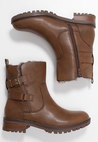 Botas de tobillo de cuero marrón con un acabado texturizado, cremalleras laterales, detalle de hebilla y borde de piel de ladrillo en el cuello. Suela de tacon grueso para mayor tracción.