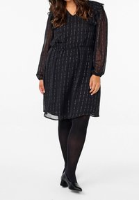 Svart klänning med genomskinliga långa ärmar, V-ringning och elastisk midja. Har ett randigt mönster av silveraccenter över hela klänningen.