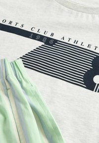 Lichtgrijze katoenen t-shirt met marineblauwe grafische tekst "SPORTS CLUB ATHLETE 1986" en gestreepte mintgroene shorts met lichtblauwe accenten.
