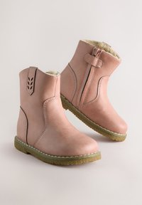 Bottines en cuir rose avec une fermeture éclair sur le côté, doublure en fourrure douce et semelle en caoutchouc texturée. Elles présentent des découpes décoratives à l'arrière.