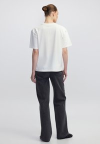 Witte T-shirt met korte mouwen en een ronde hals, gecombineerd met hooggewaisted donkergrijze wijde broek. Soepel stoftextuur, minimalistisch ontwerp.