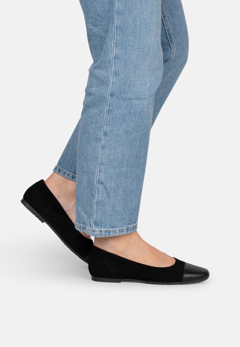 Bailarinas de ante negro con punta redonda, con una punta negra brillante y suela de goma plana, llevadas con jeans de color azul claro.