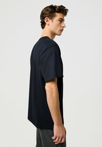 Musta puuvillateepaita lyhyillä hihoilla, pyöreällä kaula-aukolla ja rentolla istuvuudella, yhdistetty tummanharmaisiin housuihin. Yksinkertainen muotoilu, ei näkyviä kuvioita tai yksityiskohtia.