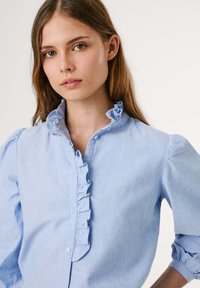 Lichtblauw shirt van katoen, met een gerimpelde kraag en knoopsluiting. Lange pofmouwen met een gathered detail.