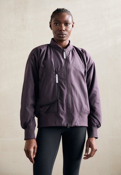 Lila bomber dzseki, elöl cipzárral, bordázott mandzsettákkal és egy oldalsó zsebbel, kontrasztos cipzárral. Simító anyag, laza fazonnal.