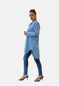 Camicia azzurra a maniche lunghe, con design a bottoni e orlo curvo. Abbinata a jeans scuri attillati e sandali neri con cinturini.