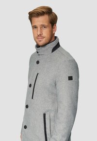 Grijze wollen blend jas met een hoge kraag, zwarte accenten, dubbelzijdige knopen en schuine voorkreukzakken. De textuurstof toont een visgraatpatroon.