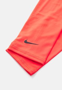 Nike atletiske leggsleeves i levende korallfarge, laget av glatt, elastisk stoff. Har en svart logo og flate sømmer for komfort.