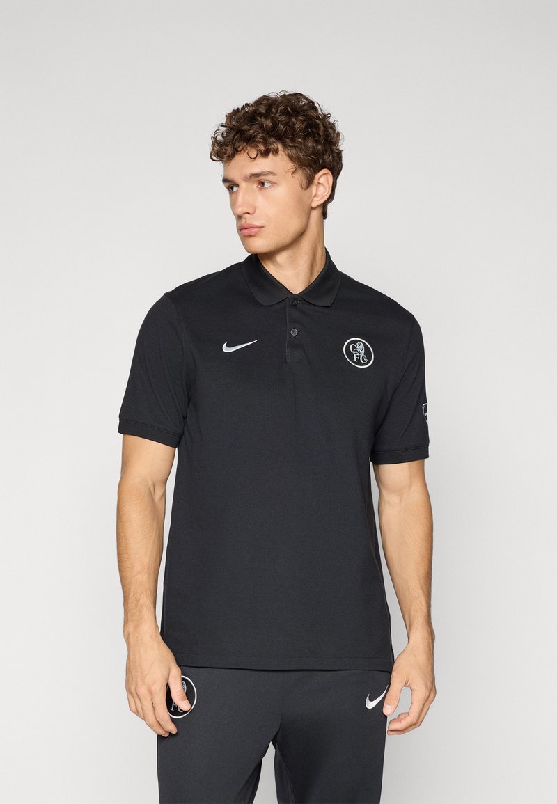 Sort polo shirt med krave, korte ærmer og Nike-logo på brystet. Har et rundt logo på venstre side. Lavet af glat stof.