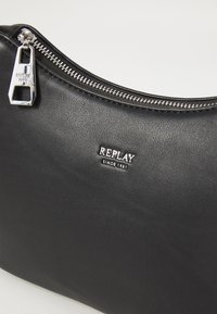 Black faux leather pouch with silver zipper and hardware. Features embossed "REPLAY" logo. Smooth texture, curved design, compact shape.