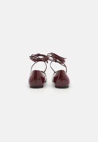 Burgundy patent leather ballet flats with a rounded toe, slender ankle straps, and flat sole. Smooth surface with minimal stitching details.