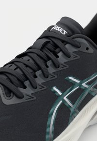 Černá sportovní bota s texturovaným materiálem, kontrastními akcenty v tyrkysové a bílé barvě, zaoblenou špičkou a integrovanými tkaničkami. Obsahuje detaily s logem na jazyku.