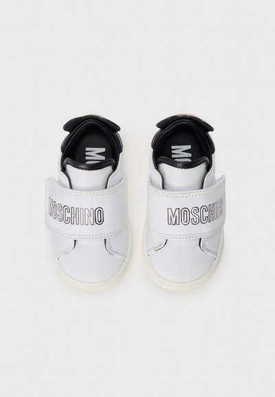 White leather children's shoes with black accents, featuring a Velcro strap with "MOSCHINO" logo and textured rubber outsole.